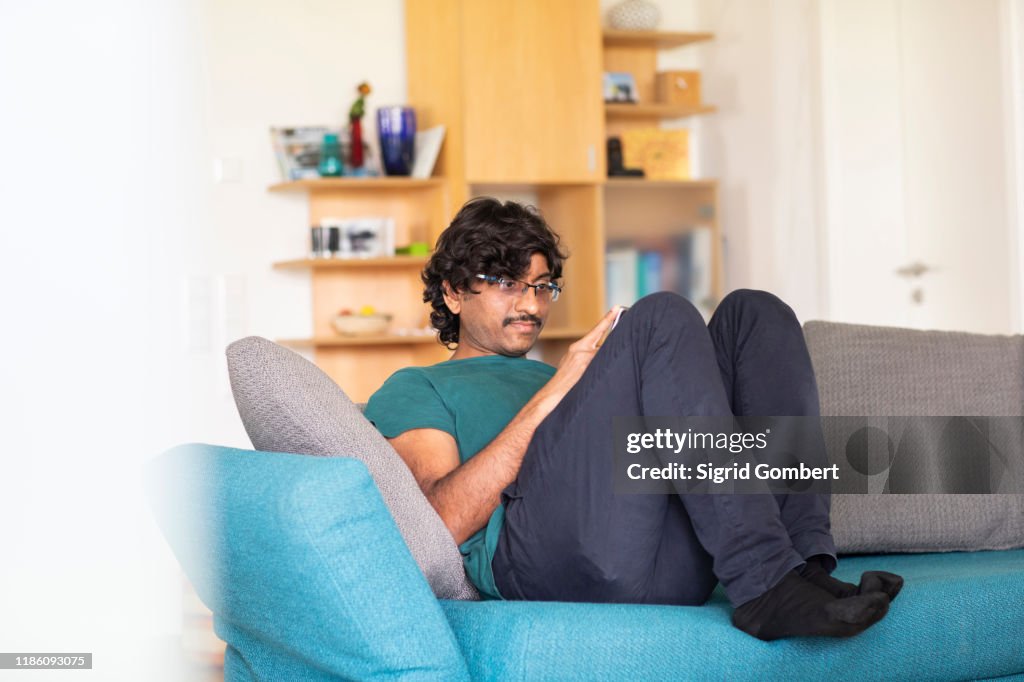 Mid adult man relaxing on sofa looking at smartphone