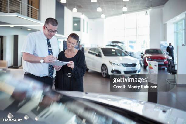 salesman discussing contract with customer in car dealership - autohändler stock-fotos und bilder