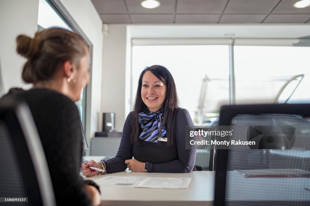 Saleswoman talking to customer in car dealership