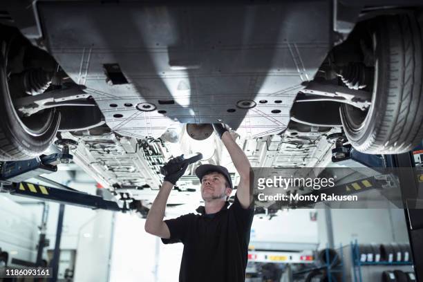 engineer working underneath car on lift in car service centre - auto repair shop stock pictures, royalty-free photos & images