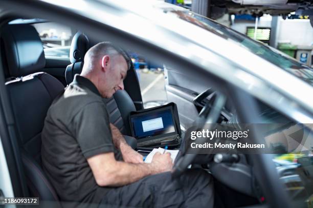 engineer using computer to check car electronics in car service centre - auto interieur stockfoto's en -beelden