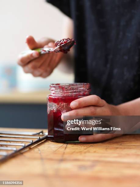 girl baking a cake, holding spoonful of jam at kitchen table, close up of hands - marmeladenglas stock-fotos und bilder