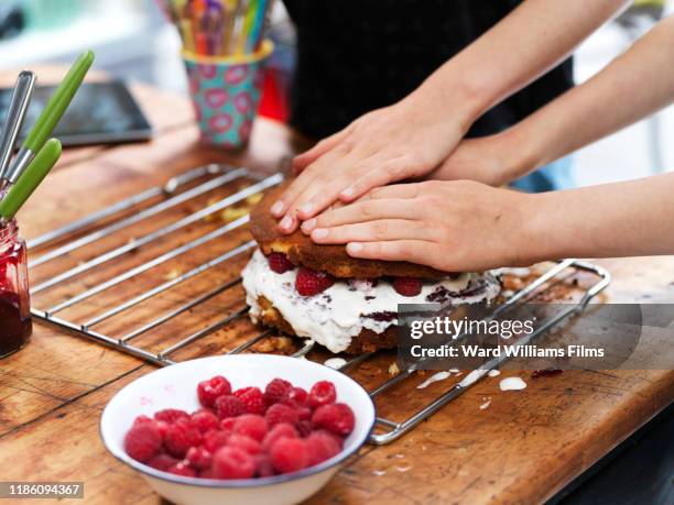 girl and her sister baking a cake, pressing down top layer at kitchen table, cropped view of hands - push cake stock pictures, royalty-free photos & images