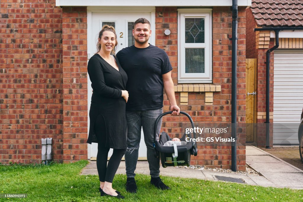 Couple carrying baby in cradle in front of house