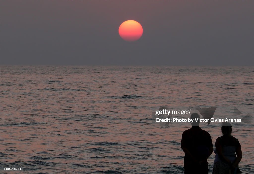 Silhouette of a backlit couple observing the sun setting on the Indian ocean, Goa, India