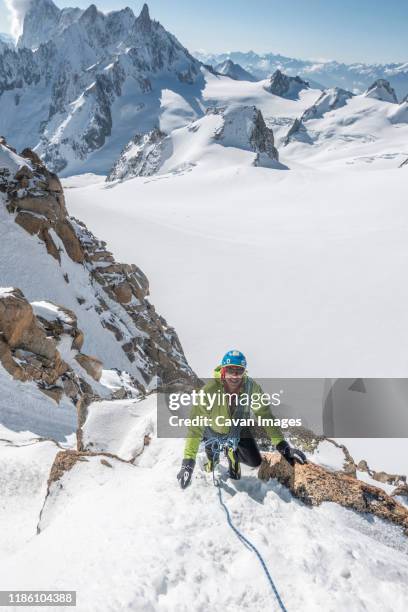 alpinist smiles as he follows up steep snow high above the glacier - aiguille du midi stock-fotos und bilder