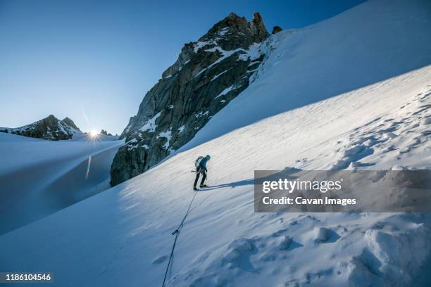 an alpinist tackles a steep snow slope as the sun crests the horizon - scialpinismo foto e immagini stock