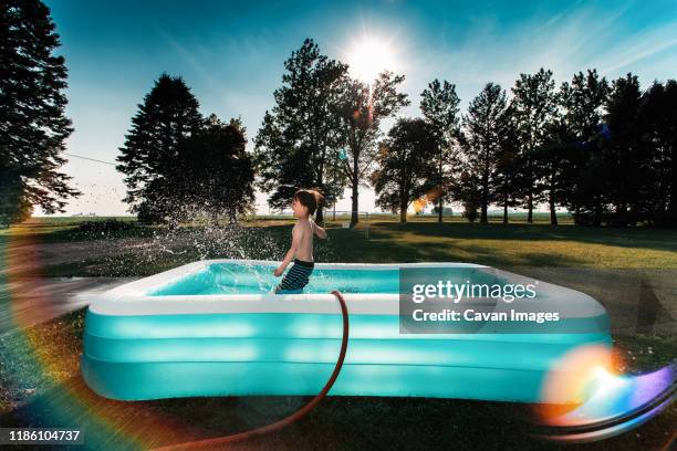 a small boy splashing water inside a swimming pool in the hot sun - inflatable swimming pool stock pictures, royalty-free photos & images