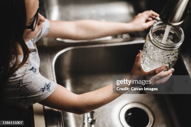 little girl fills vase with water at kitchen sink - glas heim stock-fotos und bilder