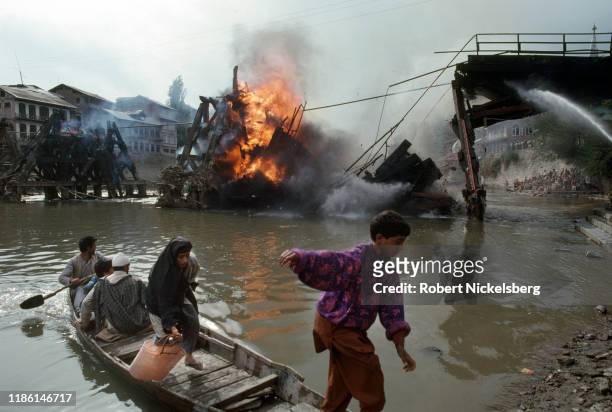 Several men, women, and children use a boat to cross the Jhelum River as the Ali Kadal bridge burns nearby, Srinagar, India, September 1, 1990. The...