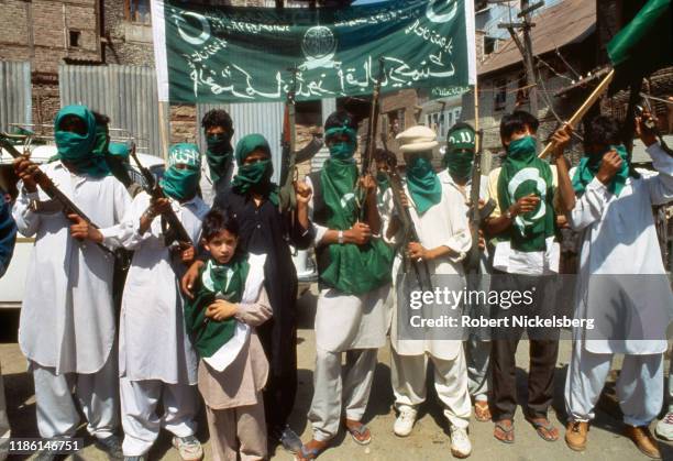 Portrait of members of the pro-Pakistan, Al Umar militant group, green scarves over most of their faces, as they pose with assault rifles and flags...