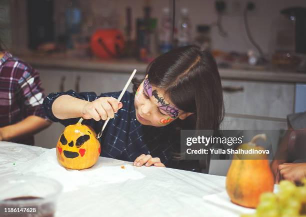 a girl with face art is painting on pumpkin at the halloween party - halloween craft stock pictures, royalty-free photos & images