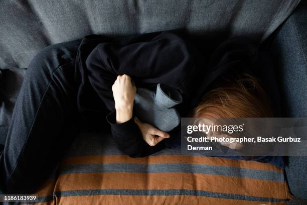 shot of a young woman suffering from stomach cramps at home - pm images stock-fotos und bilder