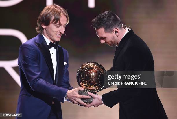 Real Madrid's Croatian midfielder and last year's Ballon d'Or winner Luka Modric gives his trophy to Barcelona's Argentinian forward Lionel Messi...