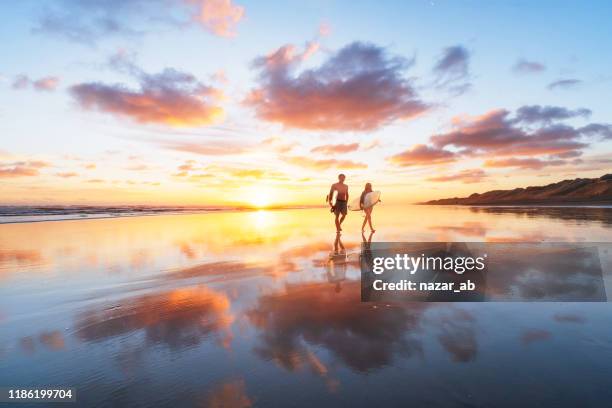 surfer couple heading back after a long day at beach. - new zealand people stock pictures, royalty-free photos & images