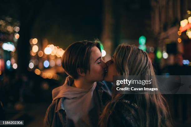 lesbian couple kissing in city at night - kussen stockfoto's en -beelden