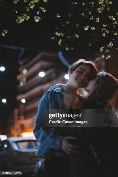 lesbian couple romancing in city while standing under a tree at night - first kiss imagens e fotografias de stock