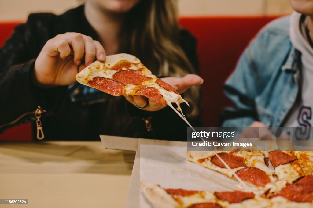 Cropped image of woman holding pizza slice at restaurant