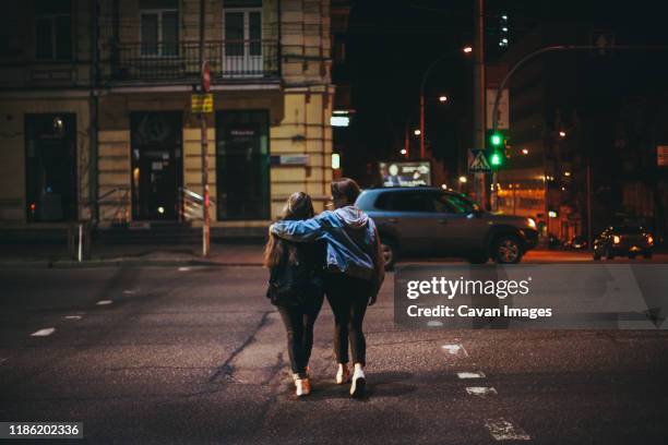 rear view of lesbian couple crossing road in city at night - couple crossing street stock pictures, royalty-free photos & images