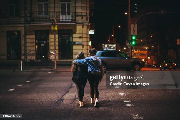 rear view of lesbian couple crossing road in city at night - ukraine city stock pictures, royalty-free photos & images