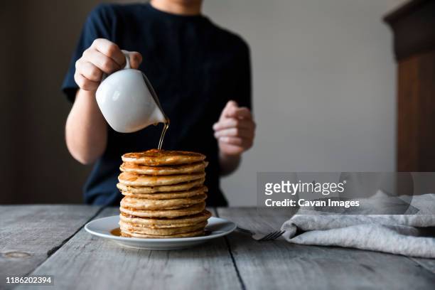 cropped shot of a child pouring maple syrup on big stack of pancakes. - maple syrup stock pictures, royalty-free photos & images