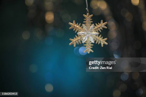 silver gold colored star-shaped christmas ornament hanging against defocused teal background - star teal stock-fotos und bilder