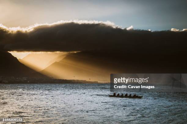 silhouette of athletes in outrigger canoe, paddle wile the sun sets. - outrigger stock pictures, royalty-free photos & images