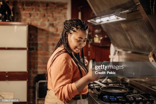 afrikanische frau mit telefon während der zubereitung von lebensmitteln - woman cooking phone stock-fotos und bilder