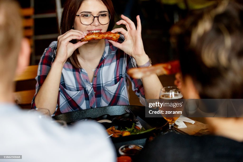 Mulher nova em um pub que aprecia o sparerib prendido nas mãos