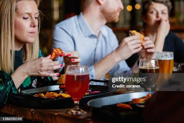 friends eating roast food held in hands and having beer - gastro pub stock pictures, royalty-free photos & images