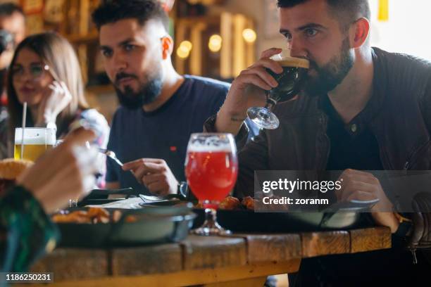 jonge man met stout ale tijdens de lunch met vrienden in een pub - artisanal food and drink stockfoto's en -beelden