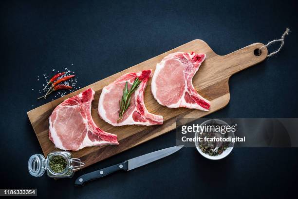 rohe schweinelendenkoteletts von oben auf dunklem hintergrund geschossen - schweinefleisch stock-fotos und bilder