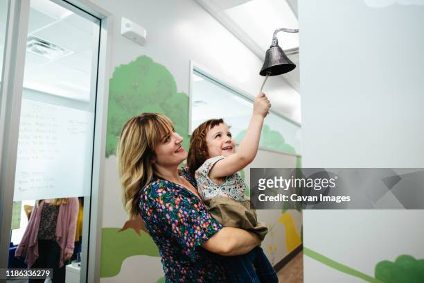 teacher holds little girl up so that she can ring a bell in a school - school bell stock pictures, royalty-free photos & images