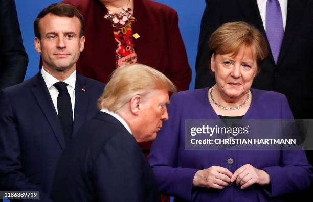 France's President Emmanuel Macron and Germany's Chancellor Angela Merkel look at US President Donald Trump walking past them during a family photo...