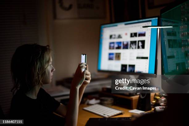 boy looking at smart phone in the dark in front of computers - android phone stockfoto's en -beelden