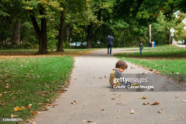 a small boy sits on a leaf-strewn path as his family walks on - tantrum stock pictures, royalty-free photos & images