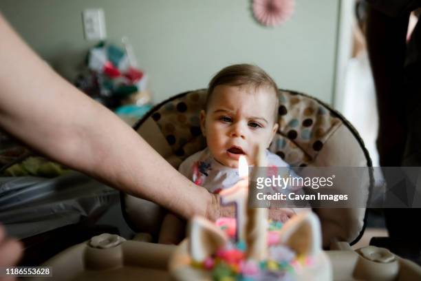 little girl at her first birthday looking at a candle on cake - eerste verjaardag stockfoto's en -beelden