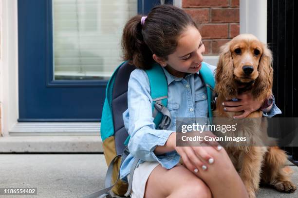 smiling girl with backpack sitting by cocker spaniel on porch - dog backpack stock pictures, royalty-free photos & images