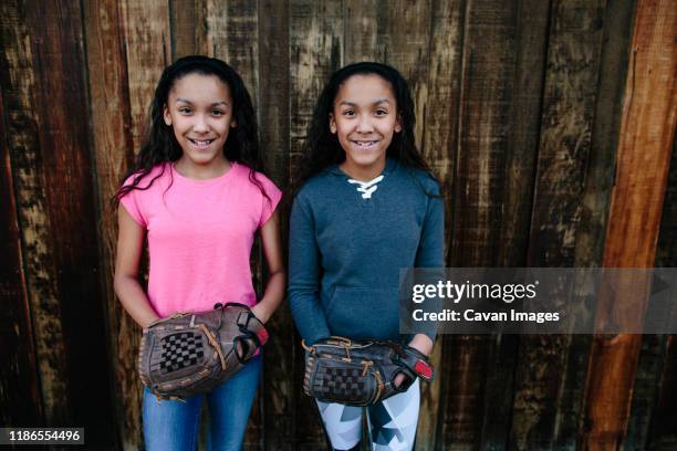 identical twin sisters stand with their softball gloves for a portrait - identical twin stock pictures, royalty-free photos & images