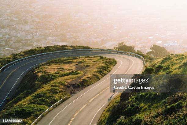 aerial view of winding road on mountain against cityscape during sunset - mountain road stock pictures, royalty-free photos & images