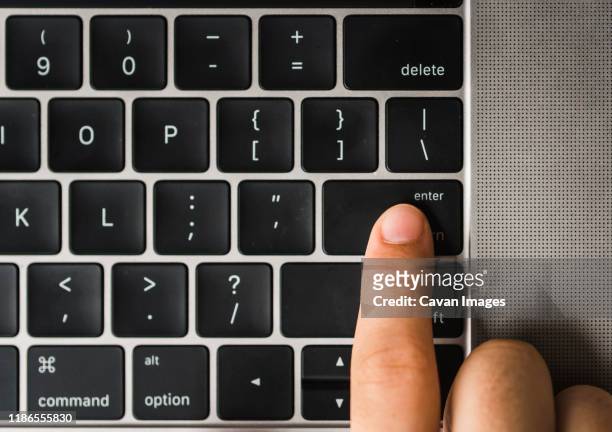 overhead view of cropped finger pressing enter key on laptop computer's keyboard - computertoetsenbord stockfoto's en -beelden
