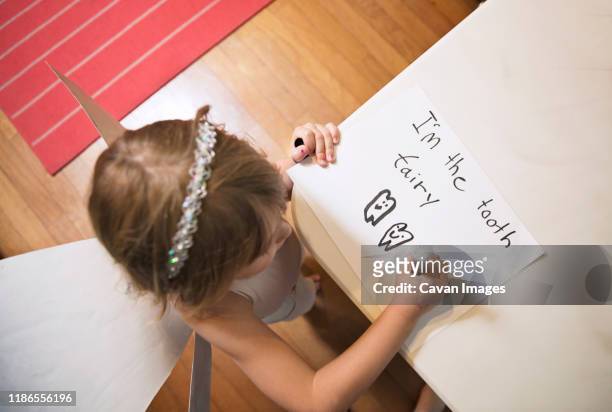 high angle view of girl wearing tooth fairy costume while writing on paper at home - tooth fairy stock pictures, royalty-free photos & images