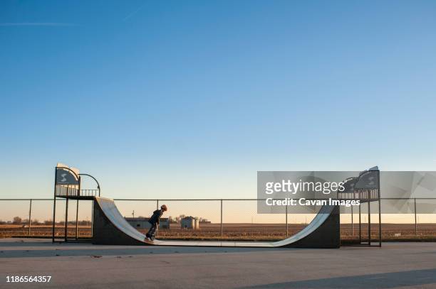 pullback of young boy riding half pipe at a skate park on sunny day - parque de skate imagens e fotografias de stock