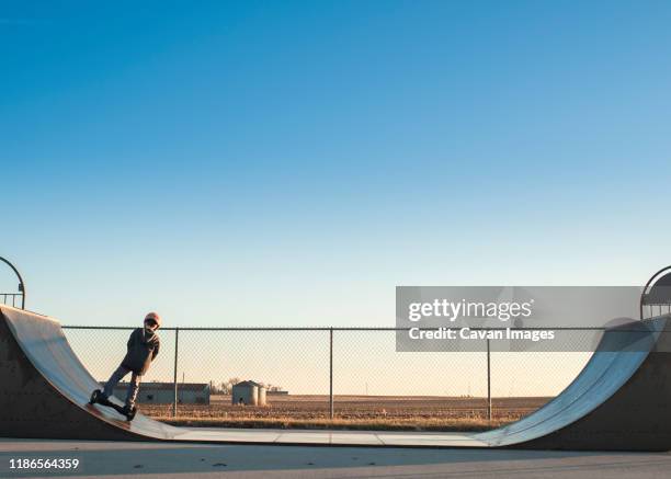 young boy using half pipe ramp at the skate park on sunny day - half pipe stock-fotos und bilder