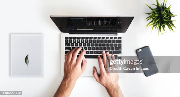 cropped image of man with mobile phone and potted plant using laptop computer on white background - raised finger stock-fotos und bilder
