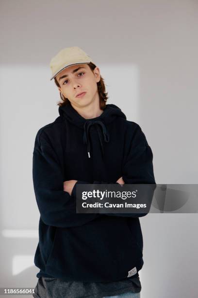 portrait of confident man with arms crossed standing against white wall - kapuzenoberteil stock-fotos und bilder