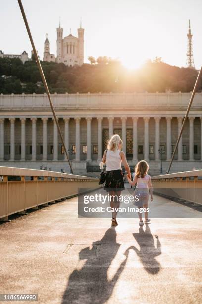 rear view of mother with daughter walking on palais-de-justice footbridge against sky during sunset - lyon france stock pictures, royalty-free photos & images