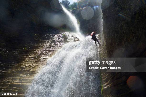 low angle view of male hiker rappelling on canyon amidst waterfall - rápel fotografías e imágenes de stock