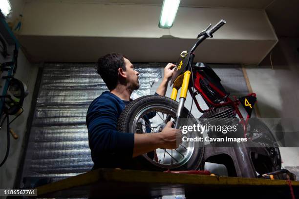 low angle view of artisan repairing motorcycle at garage - 4 wheel motorbike stock pictures, royalty-free photos & images