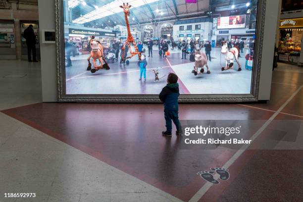 As young child is captivated by a large screen showing an augmented reality world of the station concourse and fantasy creatures, part of a loop of...